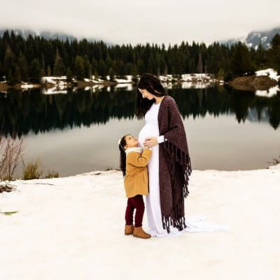Sweet daughter touching her mothers pregnant belly in the snow at Gold Creek Pond in Washington.