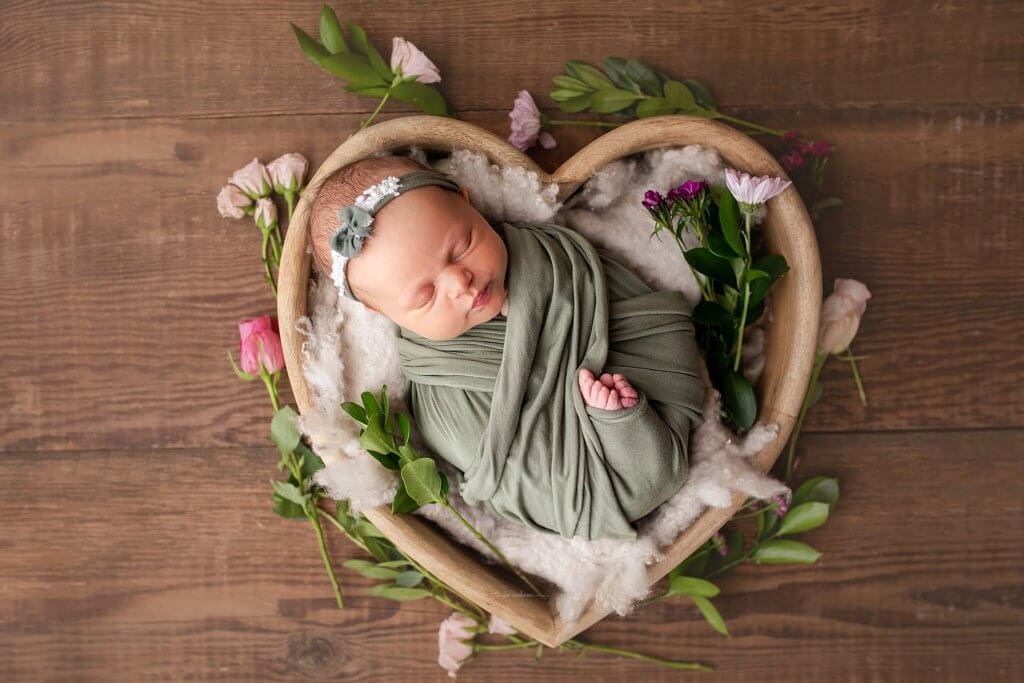 Newborn girl in heart bowl surrounded by flowers in studio session.